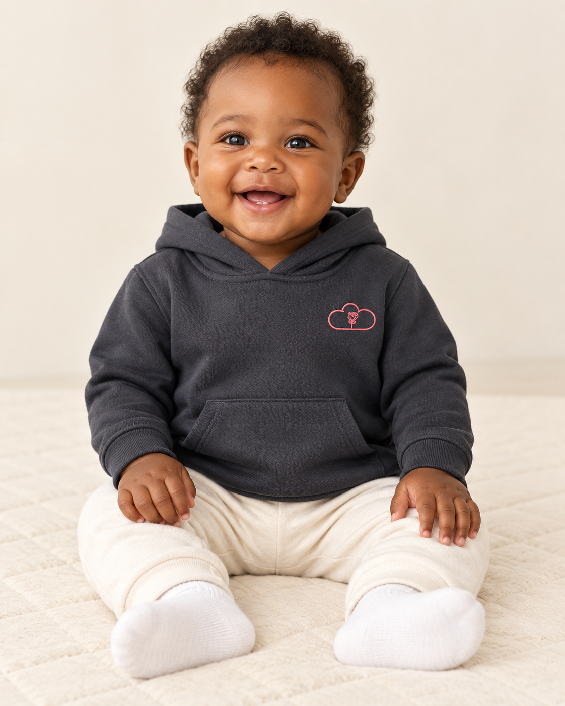 Baby wearing a black Afternoon Blossom Hoodie with a pink cloud-and-rose chest emblem.
