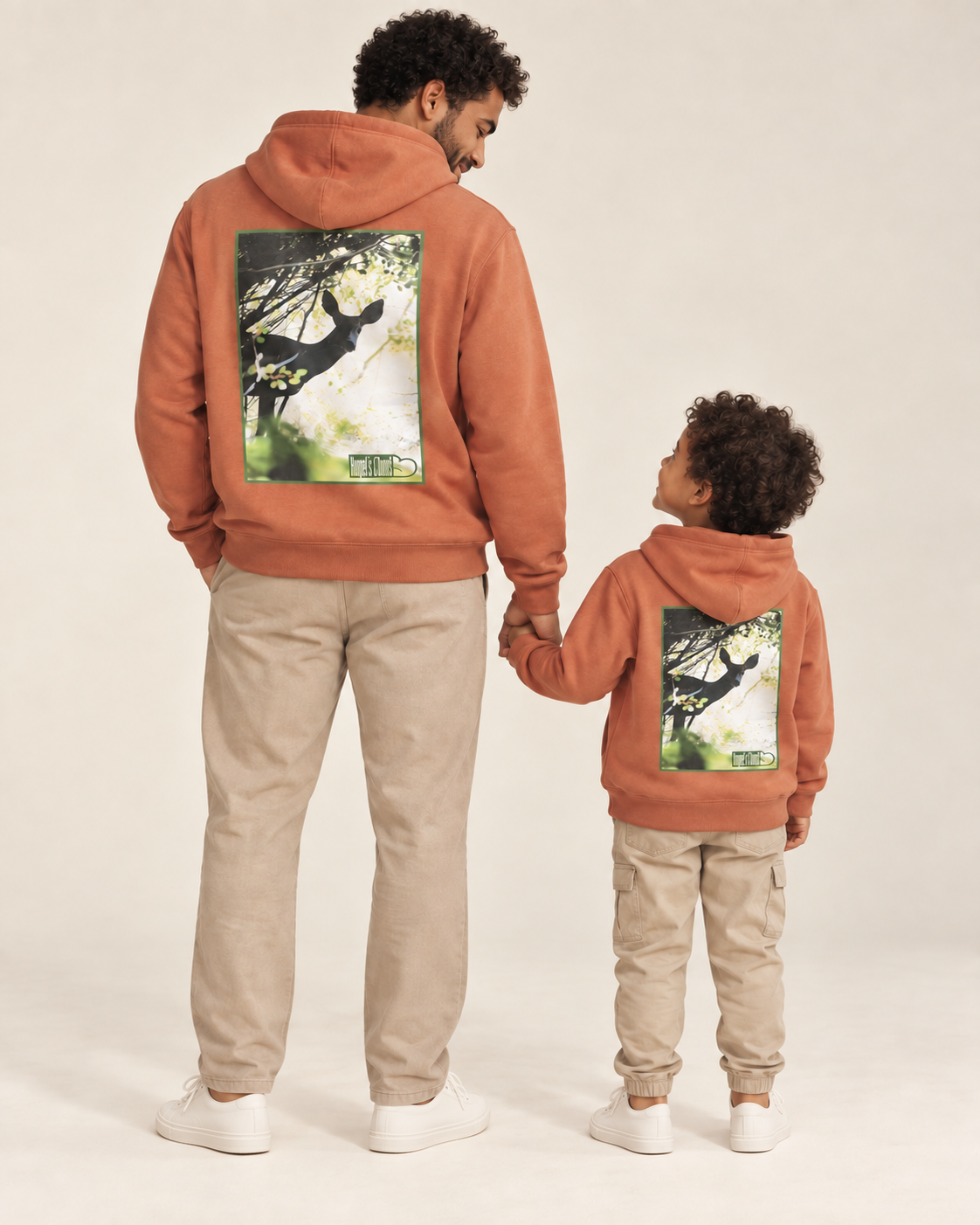 Father and child wearing matching terracotta Hunted Hoodies with green graphic details.